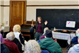 A woman in the front of a classroom holds a stringed instrument.