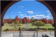 An archway opens onto a park with a flag and trees whose leaves have turned red.