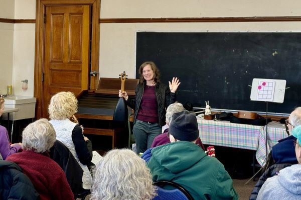 A woman in the front of a classroom holds a stringed instrument.