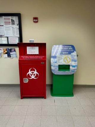 A tall red disposal container with a hazard symbol and a green container with a sign.