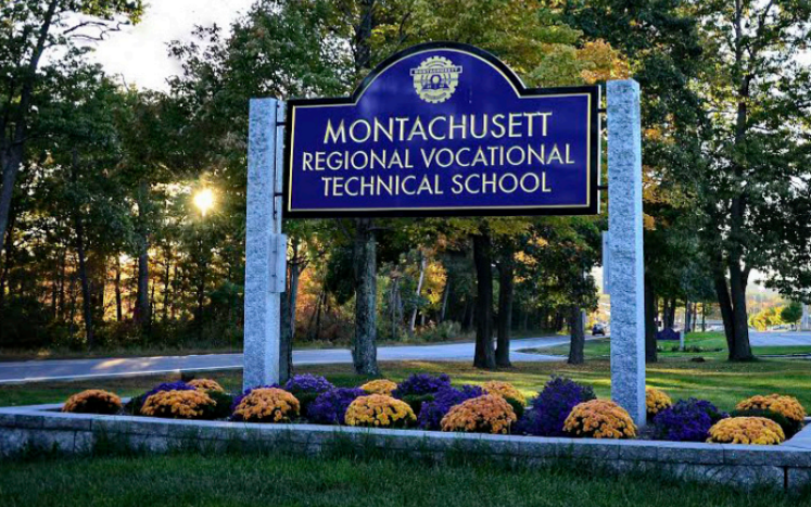 An image of the sign in front of the Monty Tech School - Blue sign with gold font on cement pillars with flowers in front of it.